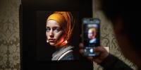 Um visitante tira foto com seu celular da imagem projetada com inteligência artificial (IA) por Julian van Dieken, inspirado na pintura de Johannes Vermeer 