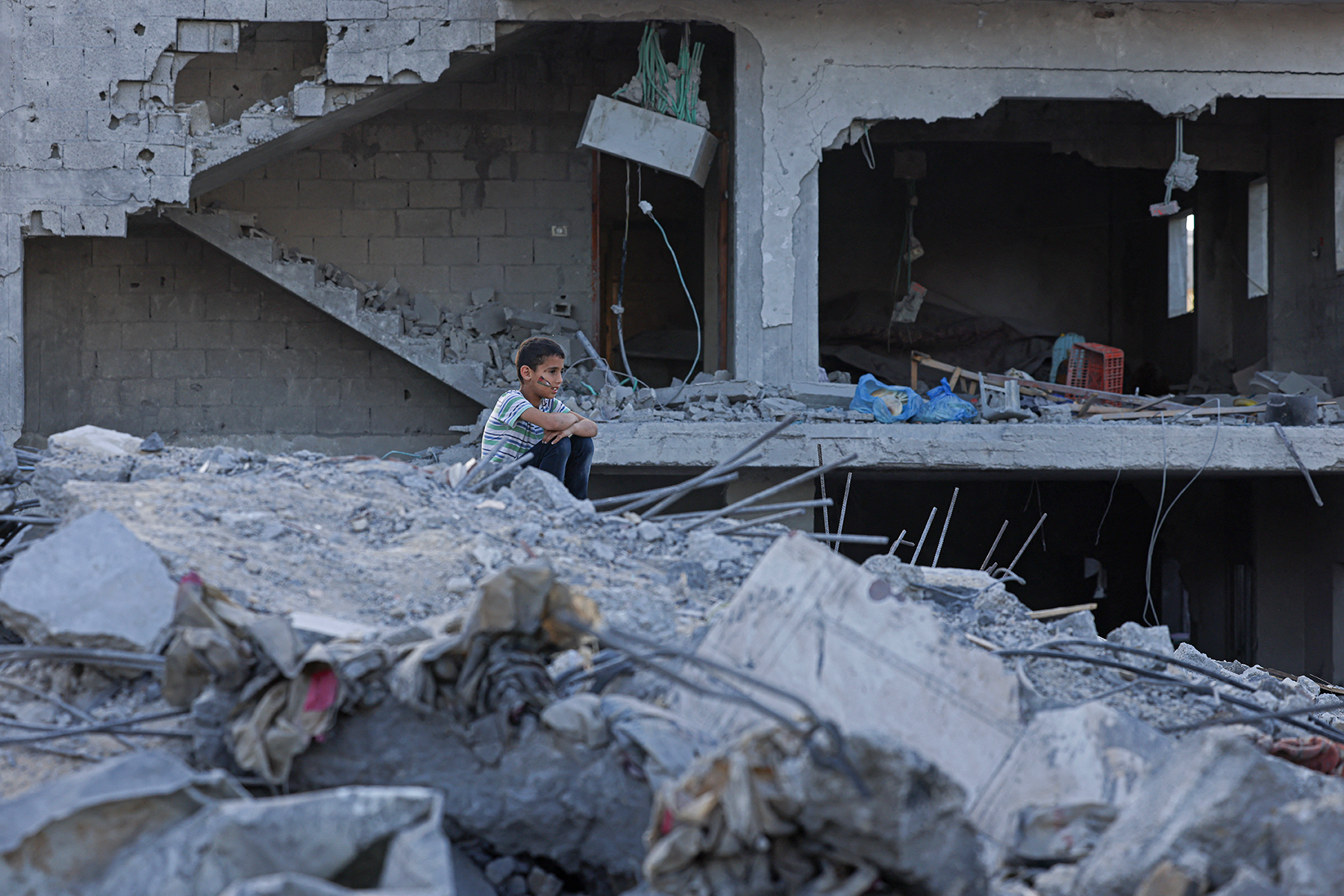 Um menino palestino senta-se entre os escombros de um pr&eacute;dio destru&iacute;do em Deir al-Balah, no centro da Faixa de Gaza, em 15 de maio de 2023, ap&oacute;s um cessar-fogo que encerrou cinco dias de combates mortais entre Israel e o grupo militante palestino Jihad Isl&acirc;mica.