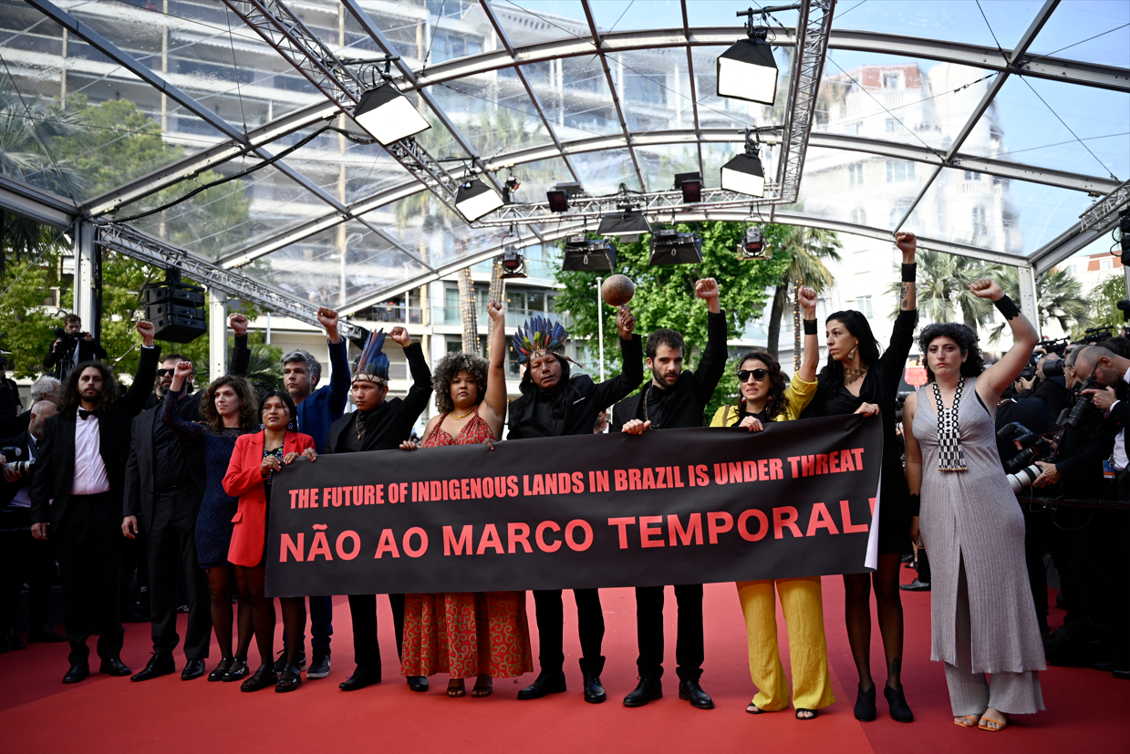 Membros do elenco do longa-metragem "Crowra" (A Flor de Buriti) e convidados atr&aacute;s de uma faixa com os dizeres " The Future of Indigenous Lands in Brazil is Under Threat / N&atilde;o ao Marco Temporal!" ao chegarem para a exibi&ccedil;&atilde;o do filme "Crowra" (A Flor de Buriti) durante a 76&ordf; edi&ccedil;&atilde;o do Festival de Cinema de Cannes