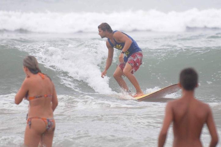 Jovens surfam, enquanto outros se banham no mar de Cap&atilde;o