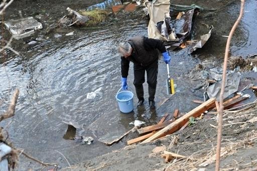 Um homem recolhe a &aacute;gua de um canal em uma cidade devastada pelo tsunami 
