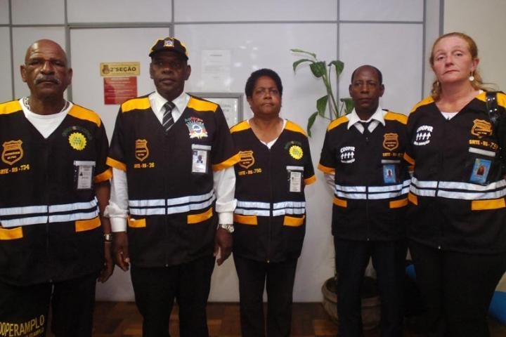 Uniforme &eacute; composto por jaleco e cal&ccedil;a pretas, com listras douradas e brancas