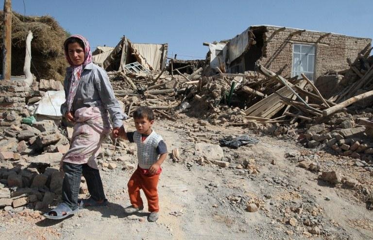 M&atilde;e e filho caminham sobre destro&ccedil;os ap&oacute;s terremoto no Ir&atilde;