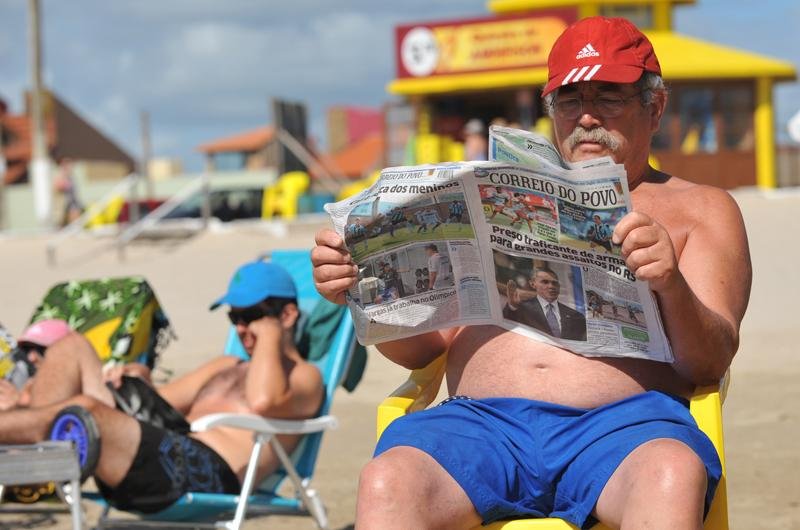 Veranista aproveita para ler jornal &agrave; beira mar