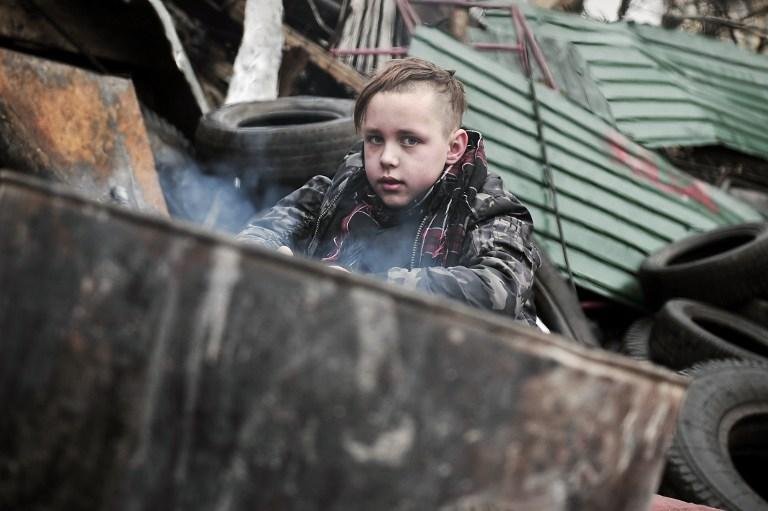 Menino se esquenta pr&oacute;ximo a uma barricada em Kiev