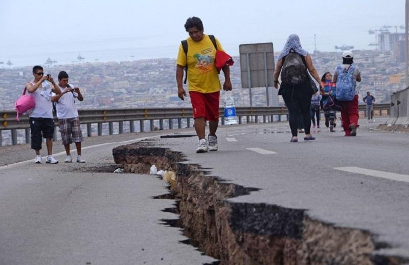 Pessoas caminham ao redor de cratera aberta por terremoto, em Iquique