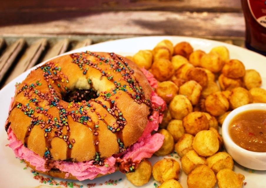 Parece um donut, mas &eacute; o Willy Wonka Burger: carne bovina, alface, cebolinha, provolone, pera caramelizada, bacon crispies e cream cheese