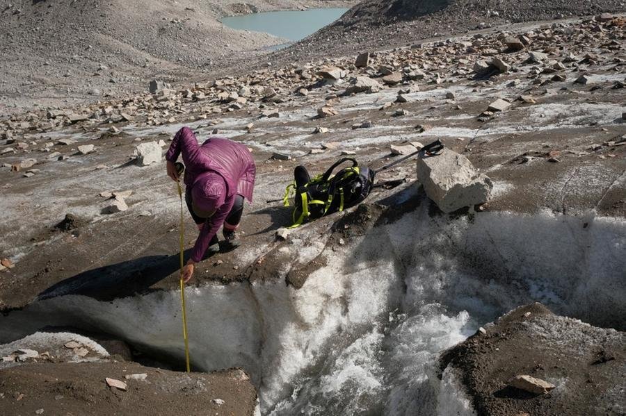 Equipada com instrumentos de medi&ccedil;&atilde;o, pesquisadora Gulbara Omorova se ajoelha &agrave; beira de uma torrente de &aacute;gua derretida