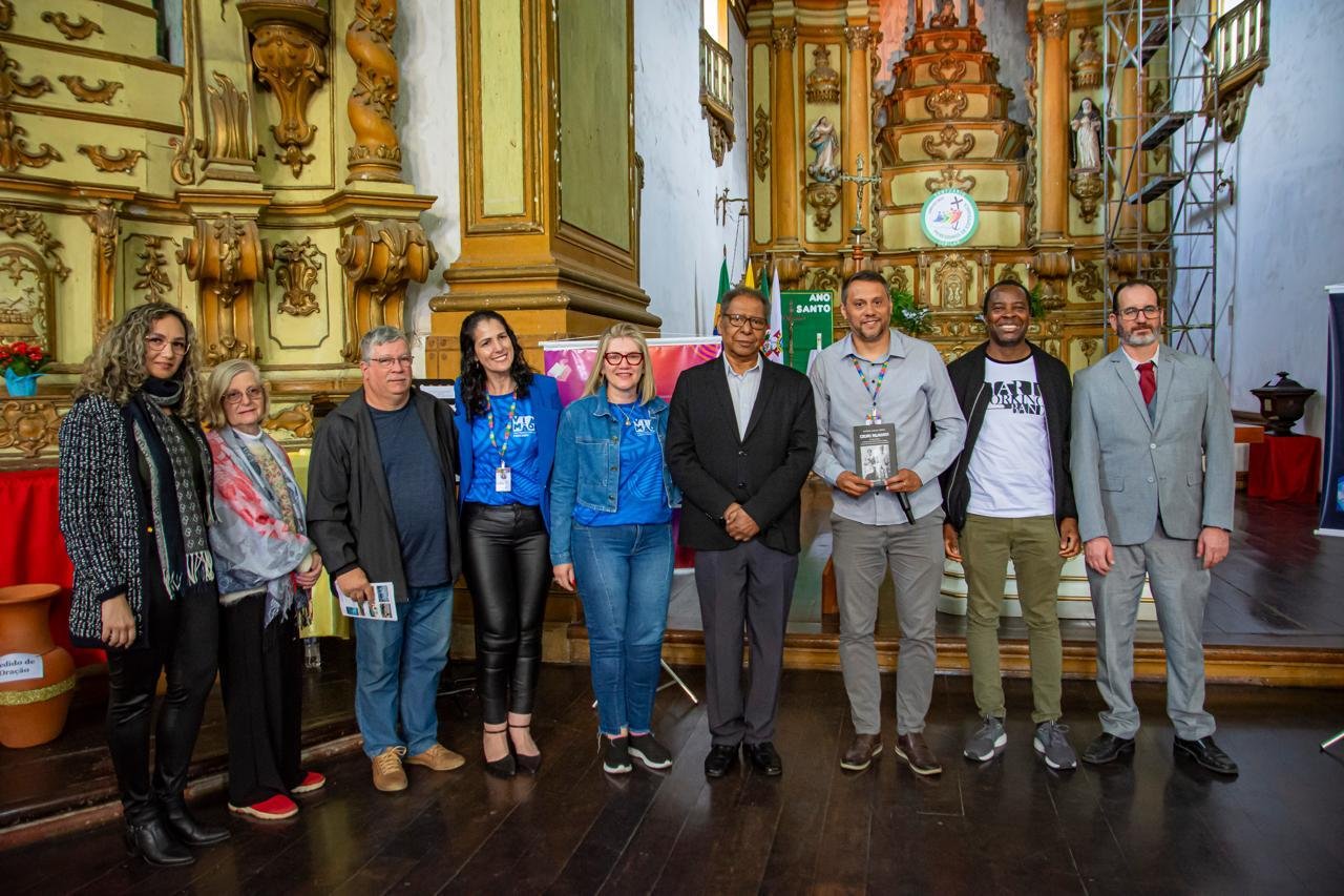 Grupo de autores com o secret&aacute;rio da Cultura, Vin&iacute;cius Santos, da secret&aacute;ria de Educa&ccedil;&atilde;o, M&aacute;rcia Culau, e do patrono da Feira Liter&aacute;ria de Viam&atilde;o, Ant&ocirc;nio Carlos C&ocirc;rtes, apresentando o conceito do livro em 2025