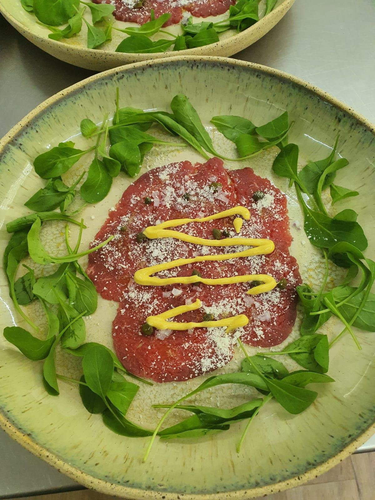 Carpaccio de fil&eacute; mignon &eacute; servido com folhas verdes, grana padano, alcaparras e molho de mostarda dijon