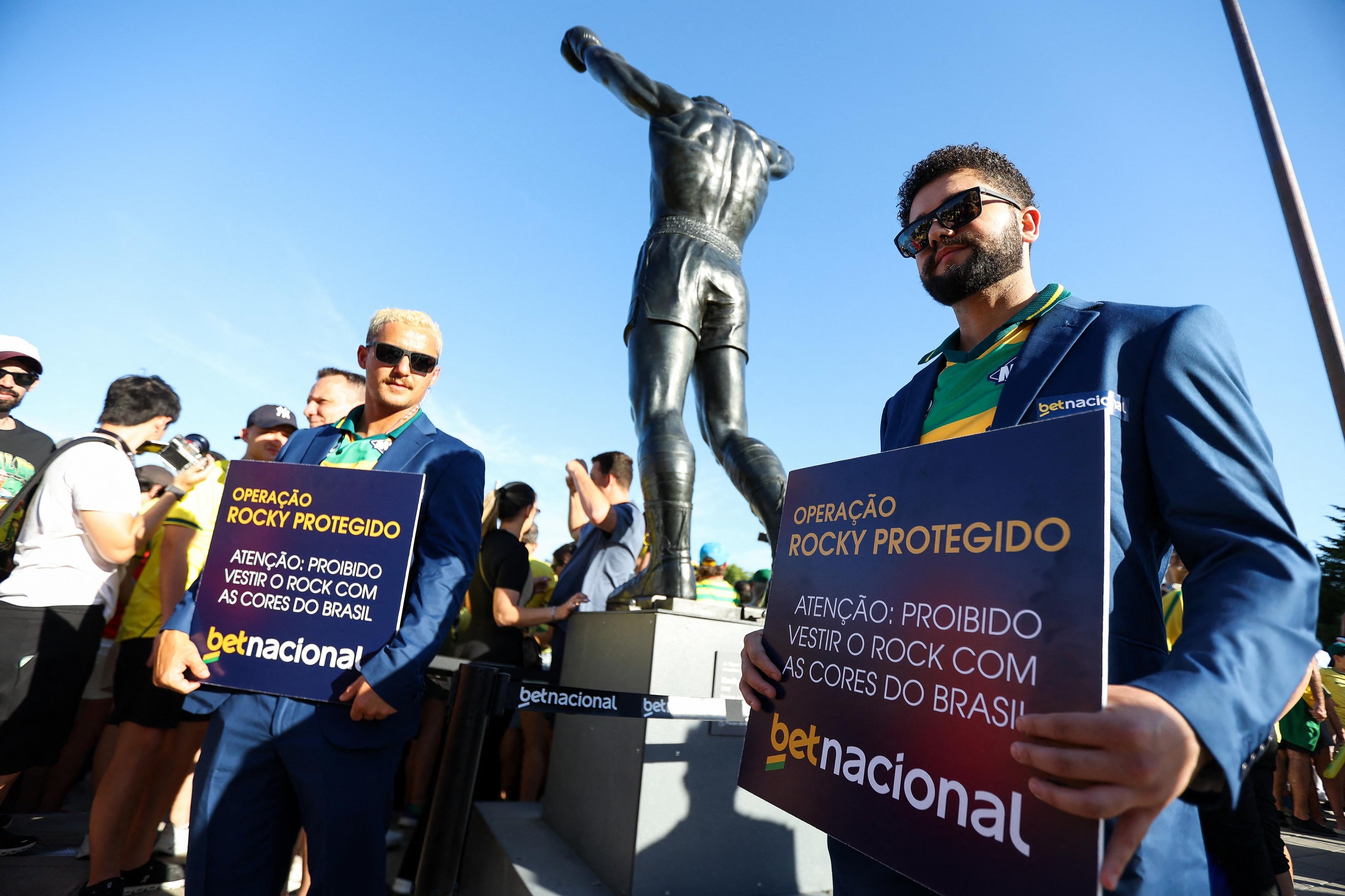 Dois brasileiros carregavam cartazes alertando que era proibido vestir o monumento do Rocky, na Filad&eacute;lfia, com as cores do Brasil