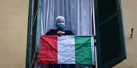 Um idoso usando uma máscara facial fica atrás de uma bandeira nacional italiana enquanto artistas se apresentam no pátio de um prédio de apartamentos popular para o show Sotto lo Stesso Cielo tour, nos subúrbios de San Basilio, em Roma