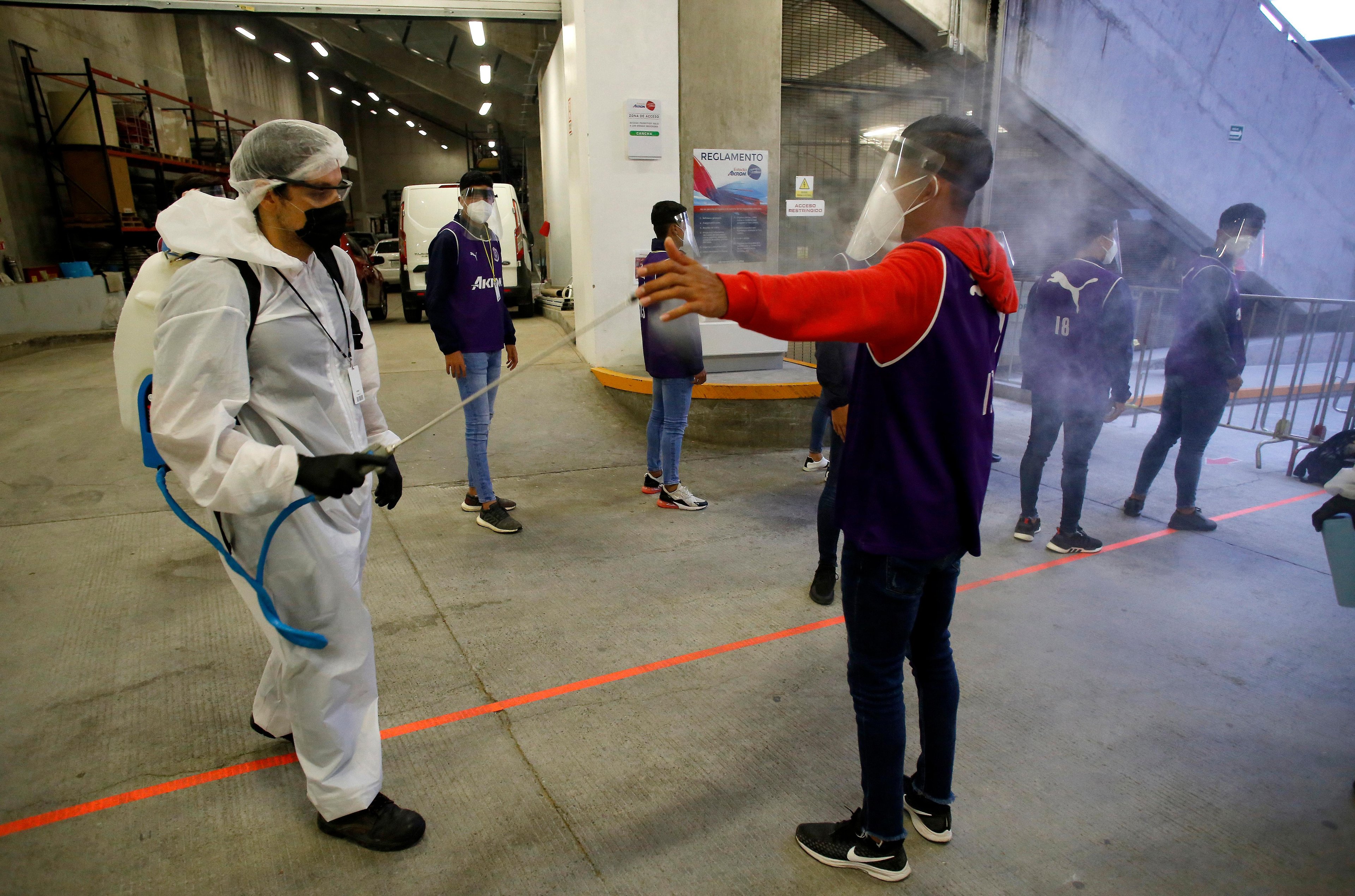 Um trabalhador desinfeta um garoto de bola antes do in&iacute;cio de uma partida de futebol de torneio mexicano entre Guadalajara e Atlas, em 4 de julho de 2020