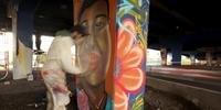 Harold Castañeda pinta o rosto de Carlota Salinas, vítima de violência, sob uma ponte em Bogotá