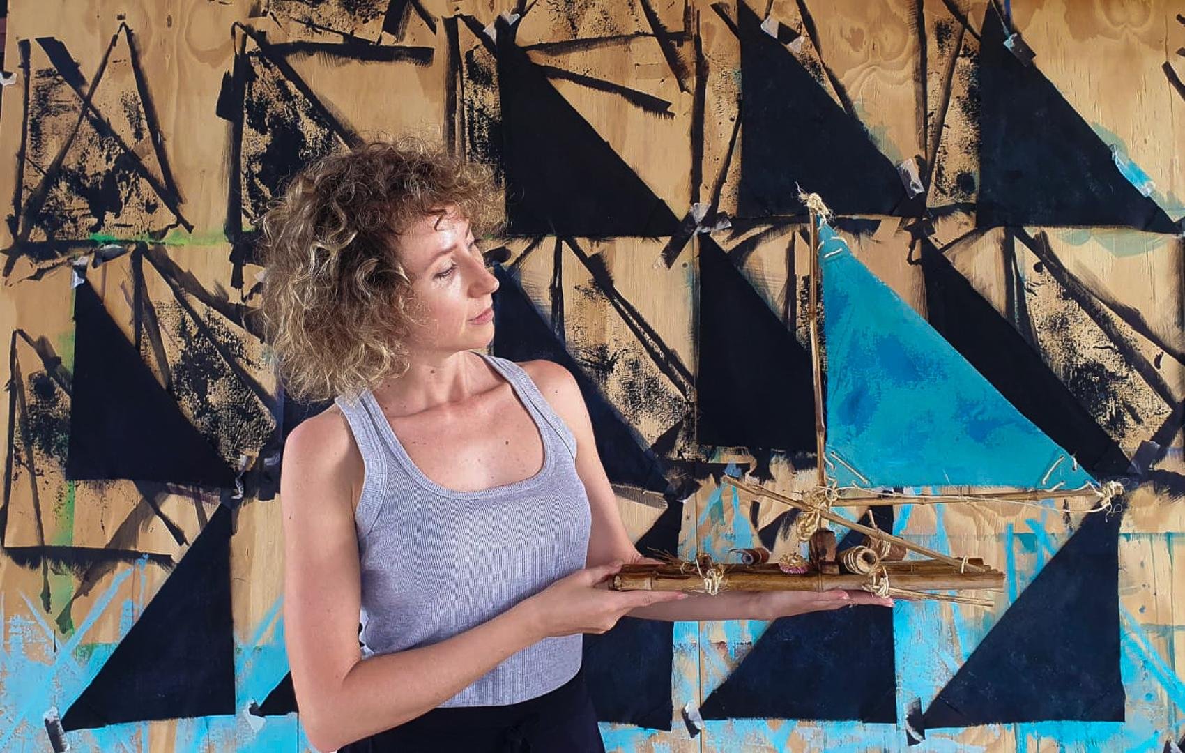 Lilian mostra uma das jangadas que refletem o c&eacute;u azul, em processo de pintura