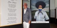 Poeta Luiz Coronel junto a banners de poema e de foto na mostra ‘Pandemias’