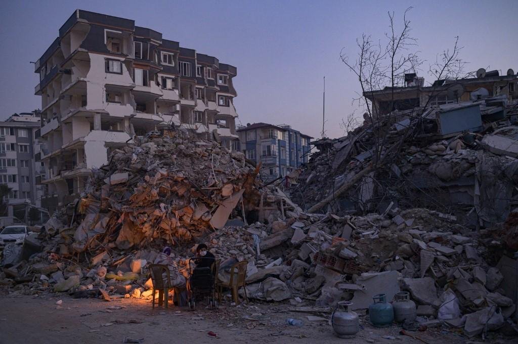 Na prov&iacute;ncia de Hatay, em frente aos escombros, duas pessoas tentam se aquecer na fogueira